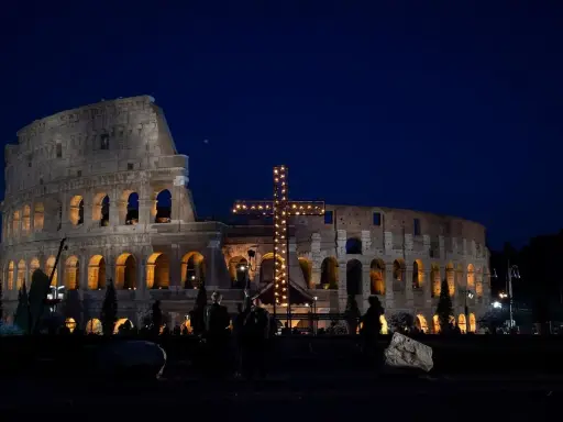 Colosseo illuminato di notte con una croce luminosa, un'atmosfera suggestiva che ricorda quando si festeggia Pasqua.
