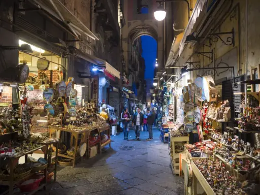 La via di San Gregorio Armeno, Napoli, illuminata di sera, con botteghe artigiane piene di presepi e statuine.