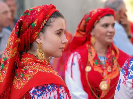 Giovani donne con foulard rossi ricamati e grandi orecchini dorati, un'immagine che evoca la tradizione di fare il portoghese con eleganza.