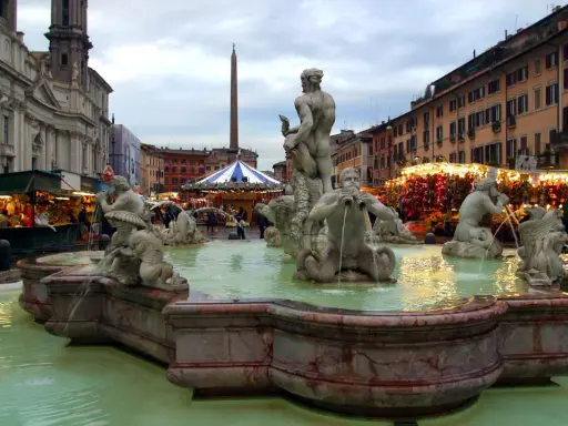 Fontana dei Quattro Fiumi a Piazza Navona, Roma, con bancarelle illuminate che anticipano quando iniziano i mercatini di Natale a Roma.