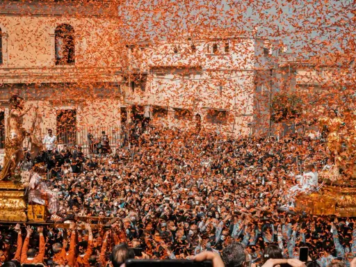 Folla festante sotto una pioggia di coriandoli arancioni, mentre si celebra cosa si festeggia a Pasqua con una processione solenne.
