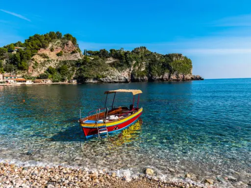 Barca colorata in un mare cristallino, ideale per scoprire cosa fare a Ferragosto in Sicilia, tra scogliere verdi e borghi pittoreschi.