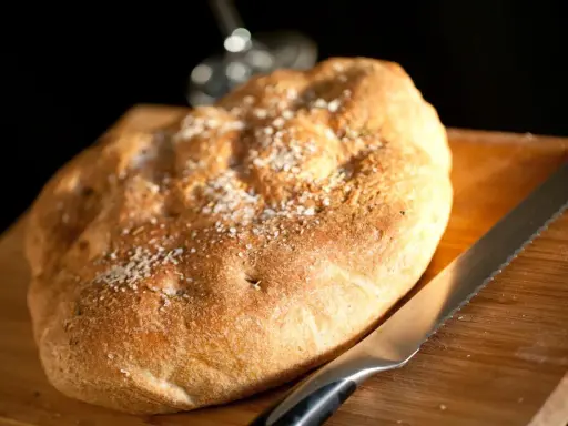 Focaccia rustica con sale grosso e rosmarino, pronta per essere tagliata. Un invito a gustare, come il pan per focaccia significato.