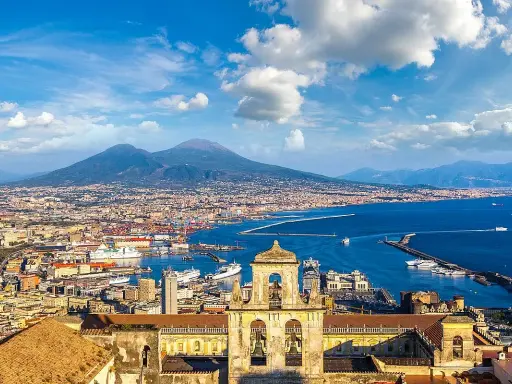 Vista panoramica di Napoli città con il Vesuvio sullo sfondo, il porto e un campanile in primo piano.
