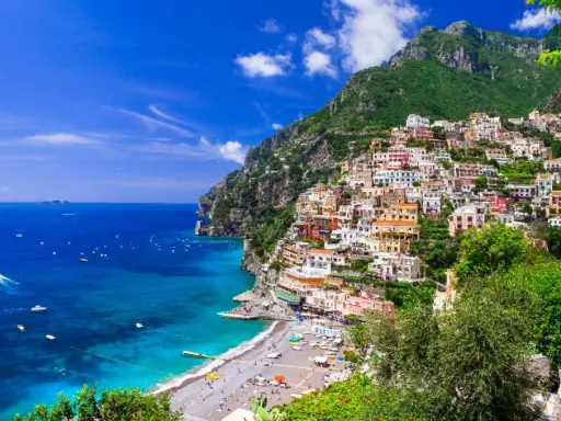 Positano, un gioiello incastonato tra il verde dei monti e l'azzurro del mare in Campania. Case colorate a picco sul mare, una spiaggia affollata e barche che solcano le acque cristalline.
