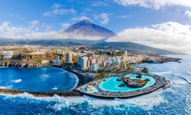 Città costiera con piscina a sfioro e vulcano sullo sfondo. Un'ottima idea su dove andare ad aprile per una vacanza al mare.