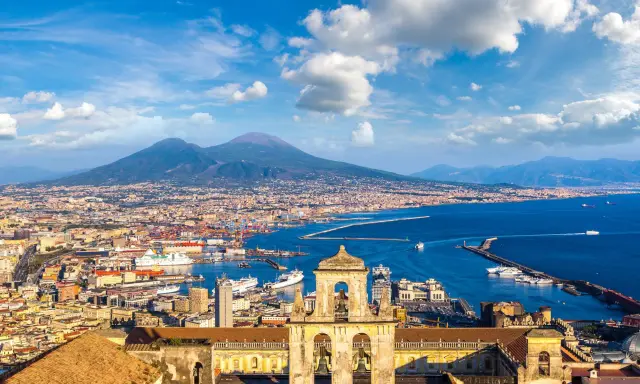 Vista di Napoli con il Vesuvio sullo sfondo, un porto vivace e un campanile antico. Un gioiello tra i siti UNESCO Campania.