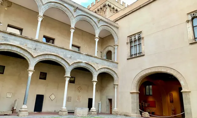 Cortile di Palazzo Abatellis, con arcate sovrapposte, finestre gotiche e opere d'arte esposte.