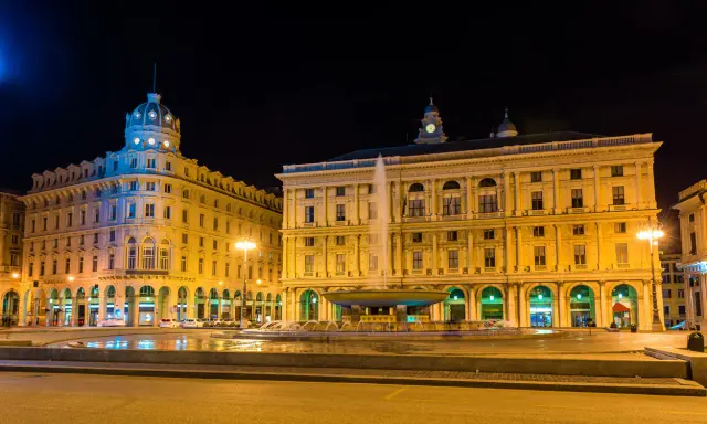 Piazza De Ferrari illuminata di notte, con la fontana centrale e gli edifici storici che animano la vita notturna di Genova.
