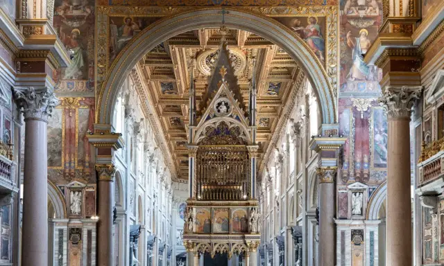 Interno di San Giovanni in Laterano: maestoso baldacchino, affreschi dorati e colonne imponenti creano un'atmosfera sacra.