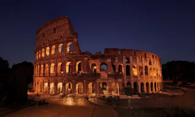 Il Colosseo illuminato di notte, con i suoi archi che creano un gioco di luci e ombre. Ci si chiede perche il Colosseo è bucato, ma la sua storia è scritta nelle sue ferite.
