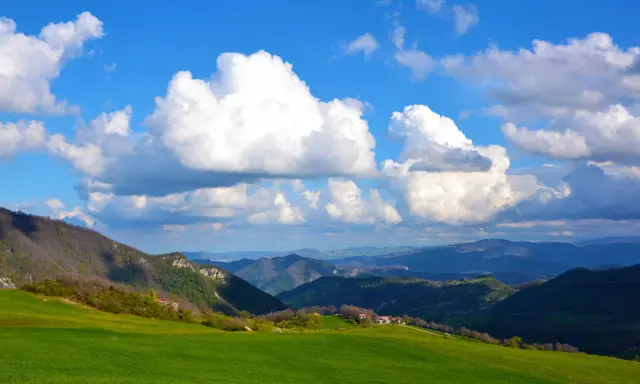 Colli bolognesi cosa vedere: verdi colline, case sparse e un cielo azzurro con nuvole bianche.