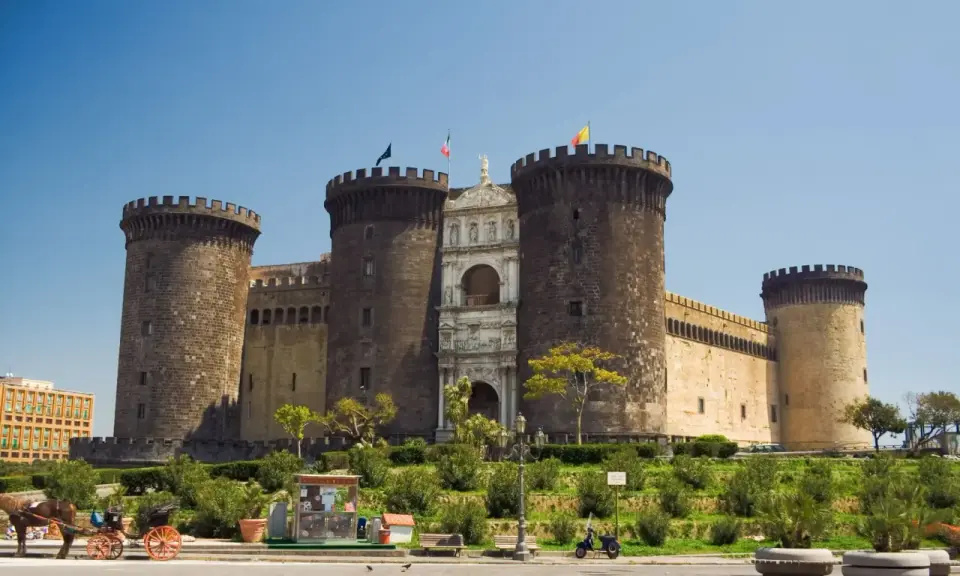 Il maestoso Maschio Angioino di Napoli, con le sue torri imponenti e l'arco trionfale, si staglia contro il cielo azzurro.