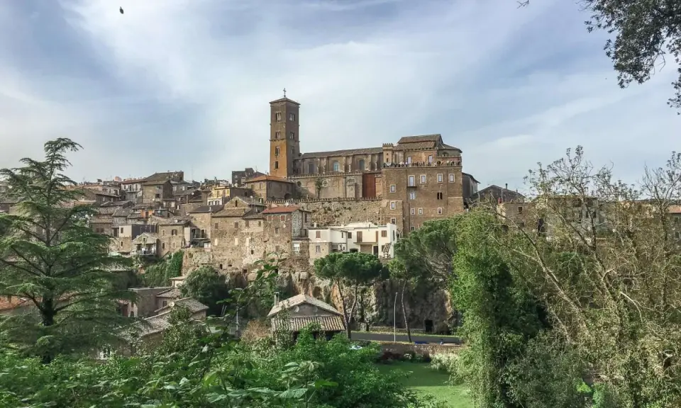Panoramica dell'antico borgo di Sutri, con le sue case in pietra arroccate su una collina e una maestosa cattedrale con campanile.