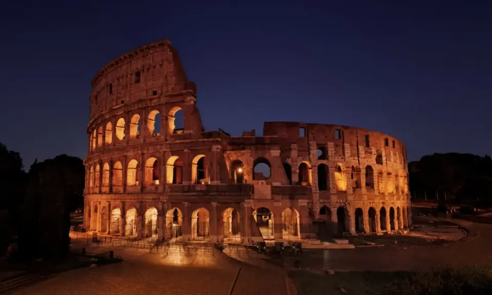 Il Colosseo illuminato di notte, con i suoi archi che creano un gioco di luci e ombre. Ci si chiede perche il Colosseo è bucato, ma la sua storia è scritta nelle sue ferite.