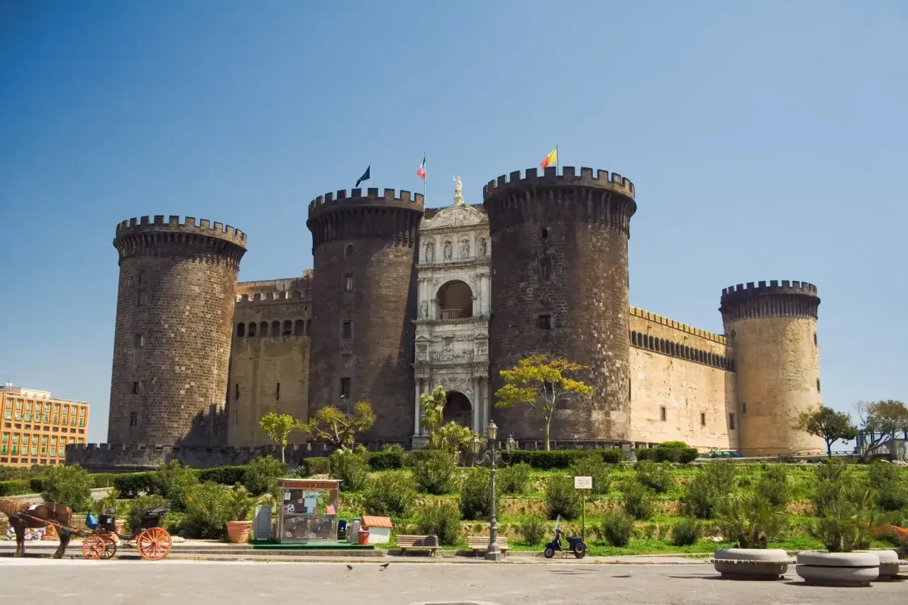 Il maestoso Maschio Angioino di Napoli, con le sue torri imponenti e l'arco trionfale, si staglia contro il cielo azzurro.