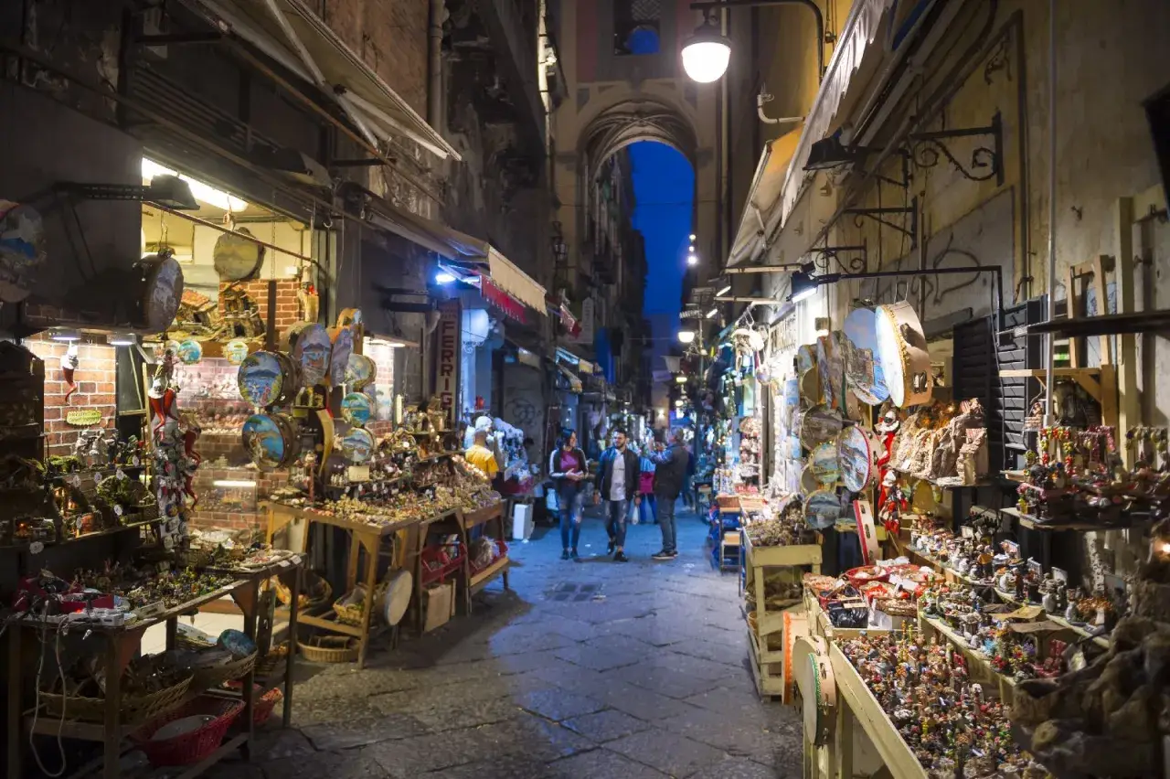 La via di San Gregorio Armeno, Napoli, illuminata di sera, con botteghe artigiane piene di presepi e statuine.