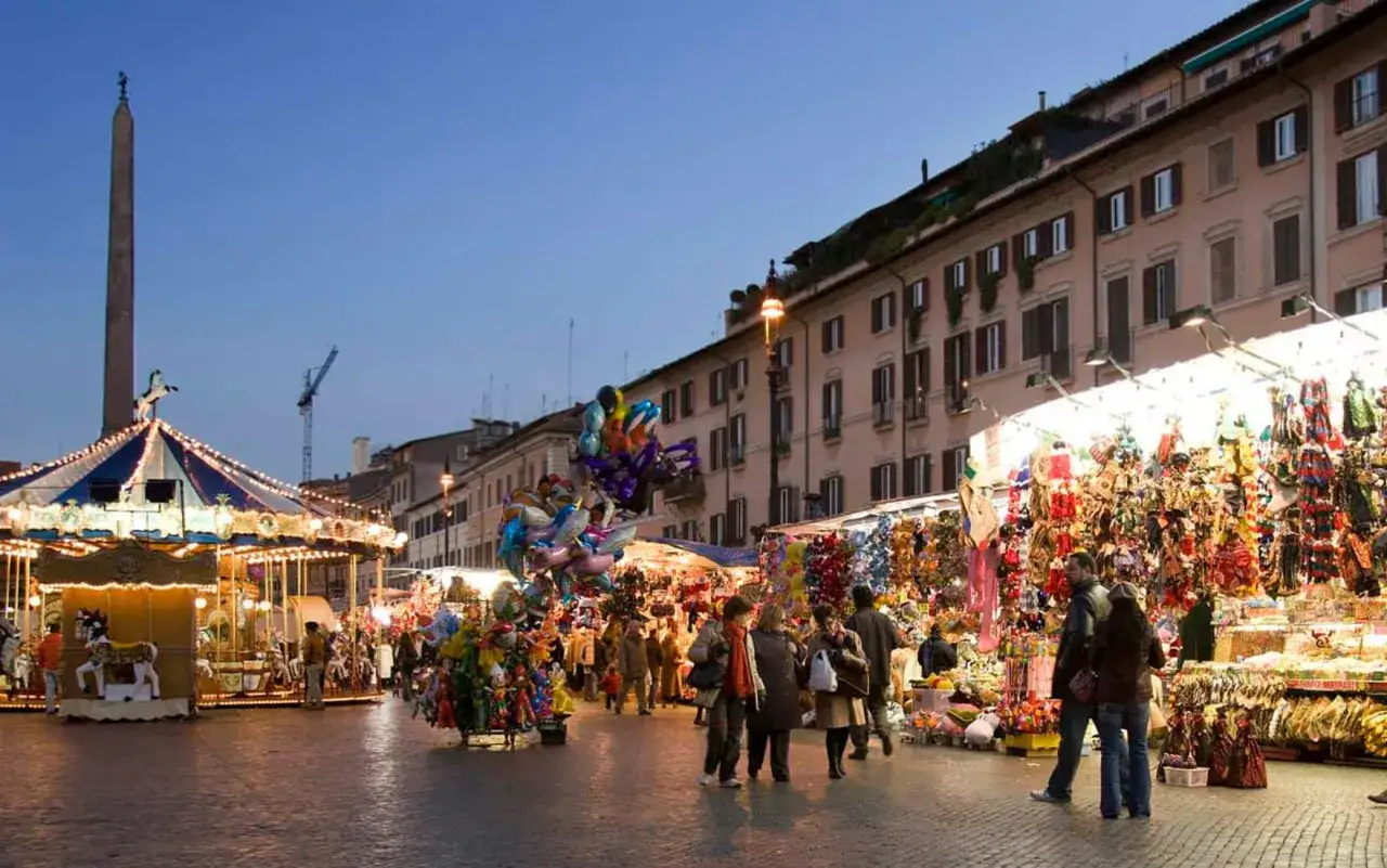 Piazza animata con giostra e bancarelle colorate, un assaggio di quando iniziano i mercatini di Natale a Roma.