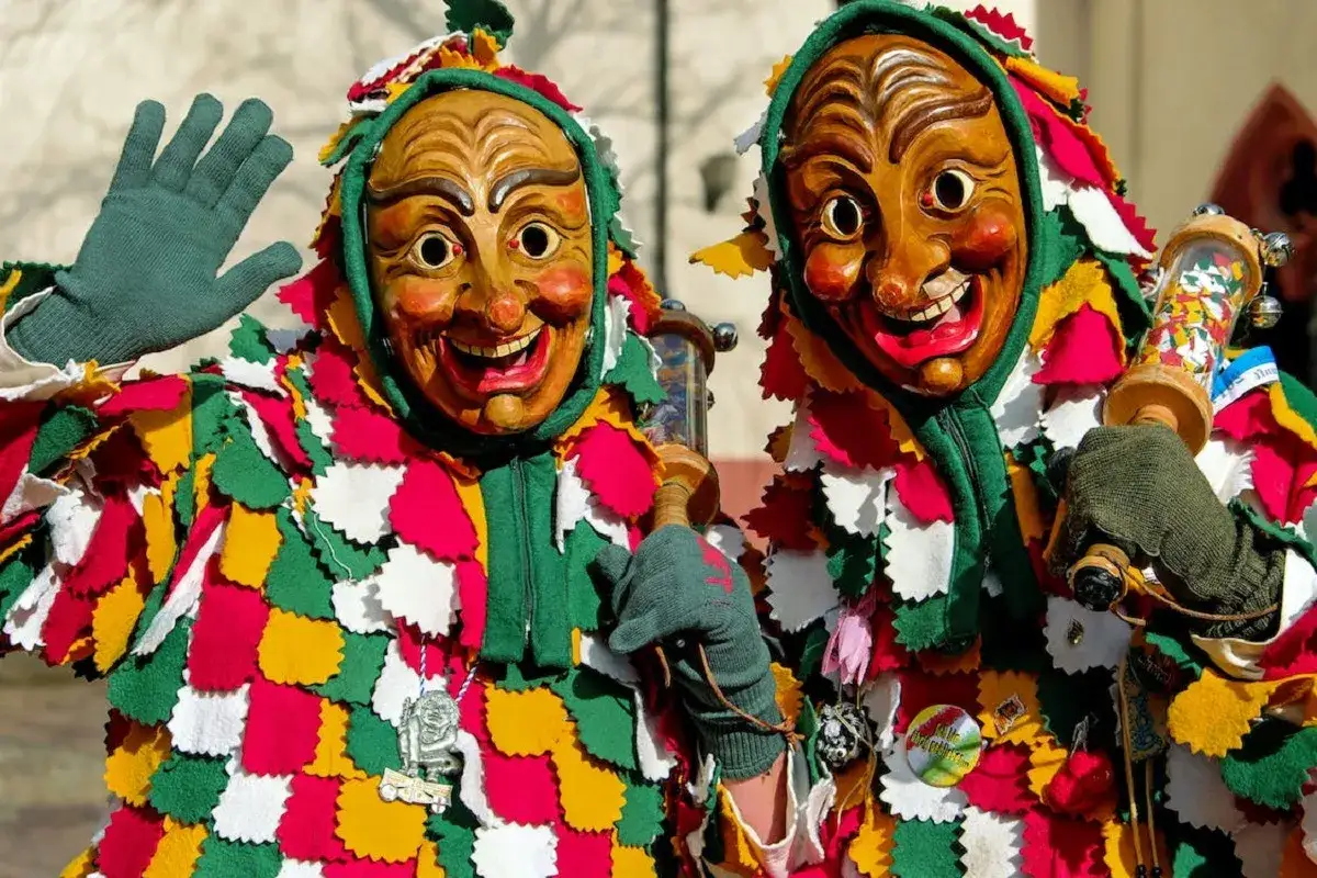 Due maschere di carnevale in Italia, con costumi colorati e volti in legno sorridenti, salutano festosamente.