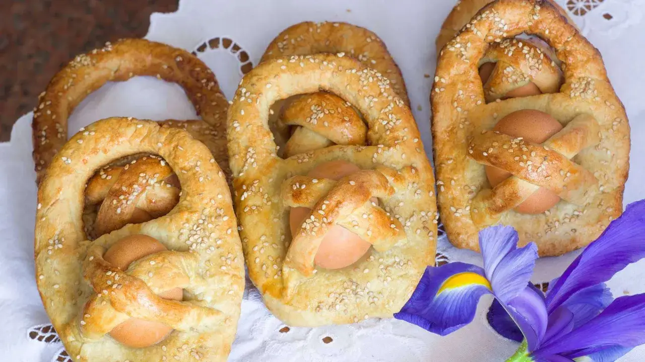 Dolci cestini di pane con uova, decorati con semi di sesamo, tipici della Pasqua in Sicilia. Un fiore viola completa la scena.
