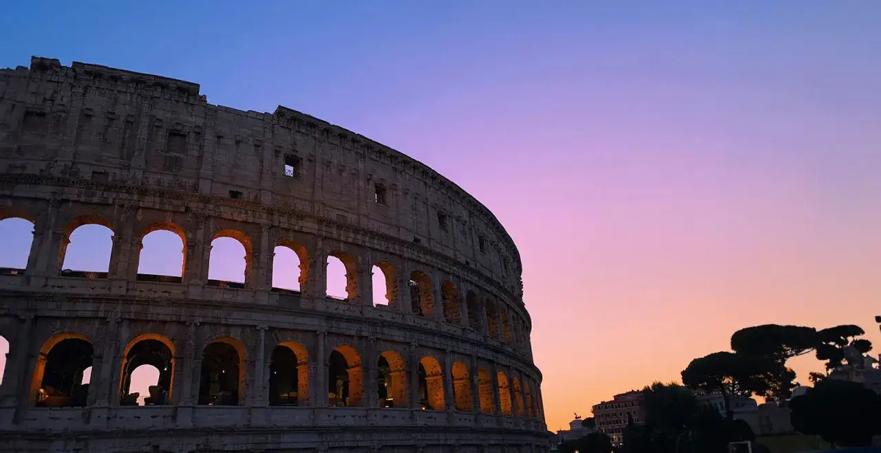 Il Colosseo illuminato al tramonto, un luogo magico dove vedere il tramonto a Roma. Il cielo sfuma dal blu al rosa.