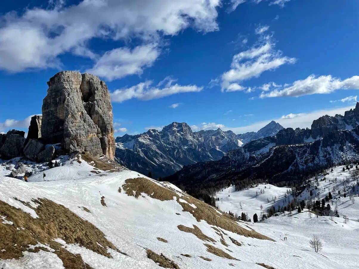 Imponente roccia nel paesaggio innevato dell'Italia del Nord, con montagne aguzze e cielo azzurro.