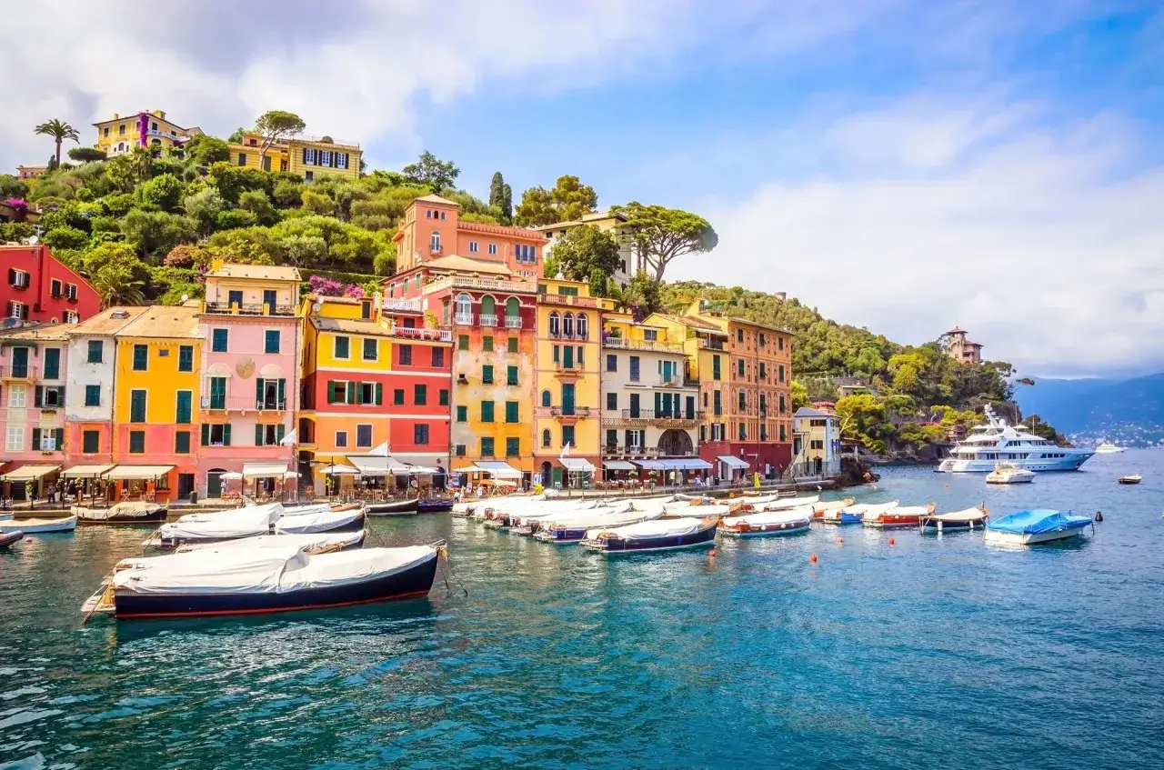 Colorate case affacciate sul mare blu della riviera ligure di levante, con barche ormeggiate e una grande yacht all'orizzonte.