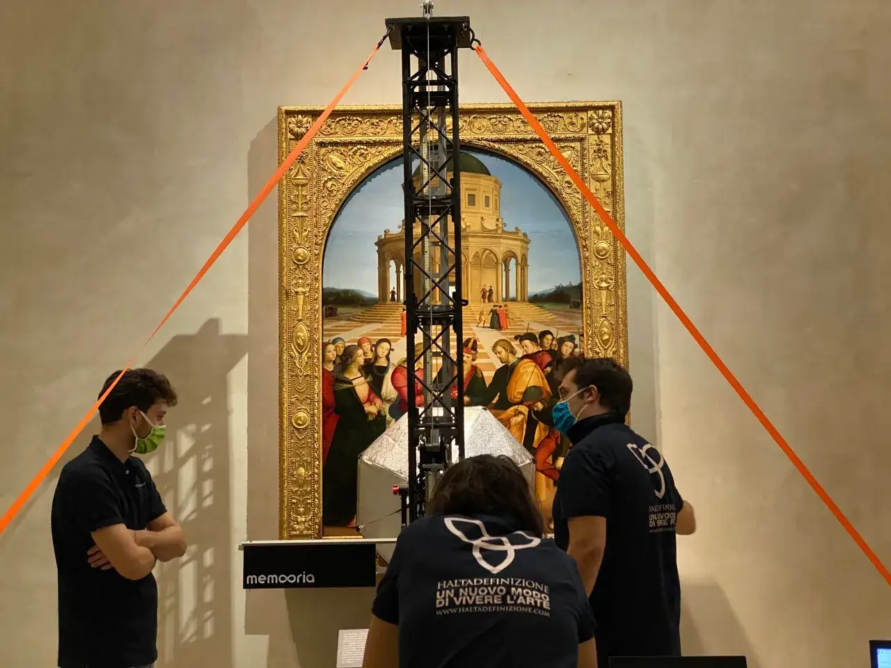 Un'installazione moderna illumina un dipinto rinascimentale, forse un'opera di Raffaello e Perugino, con persone che osservano.