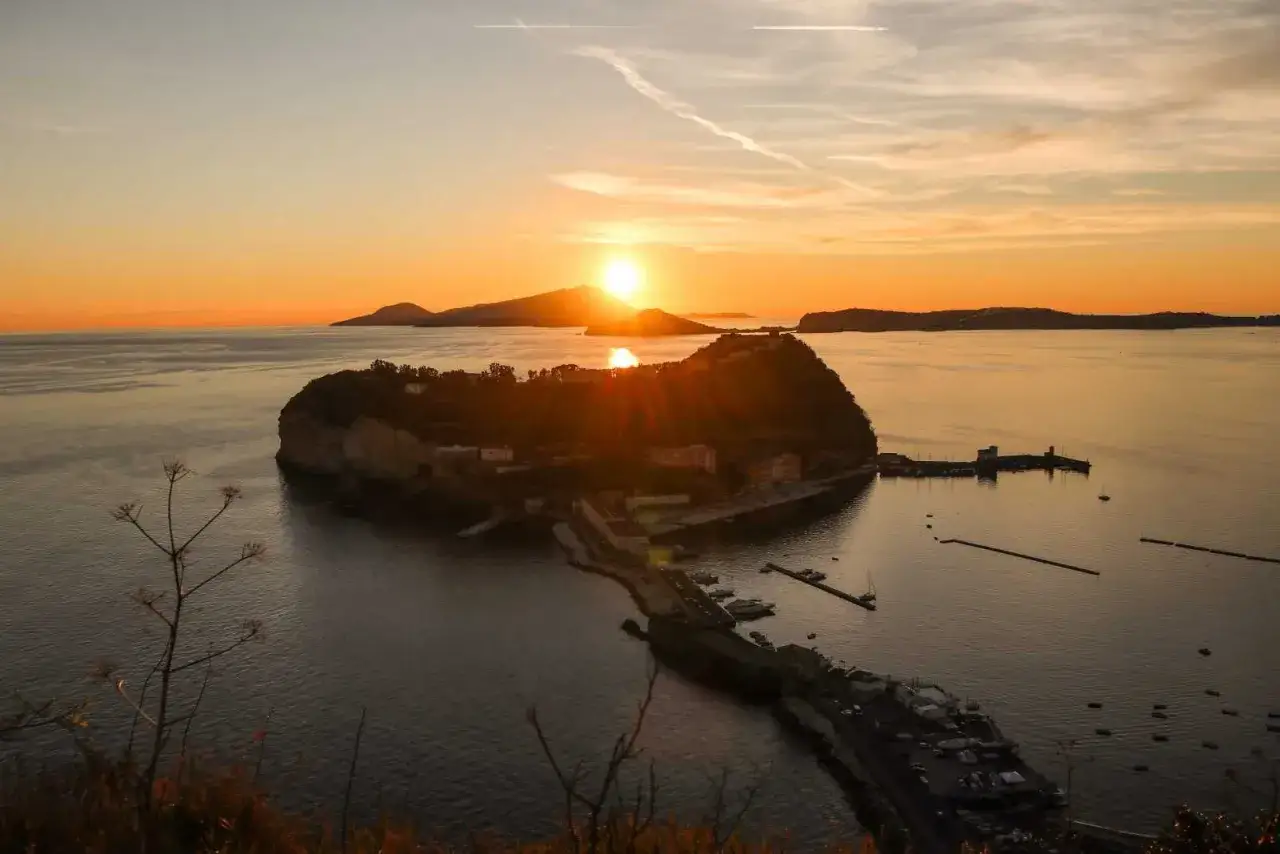 Tramonto dorato su Napoli, mare bello e un'isola con un castello.