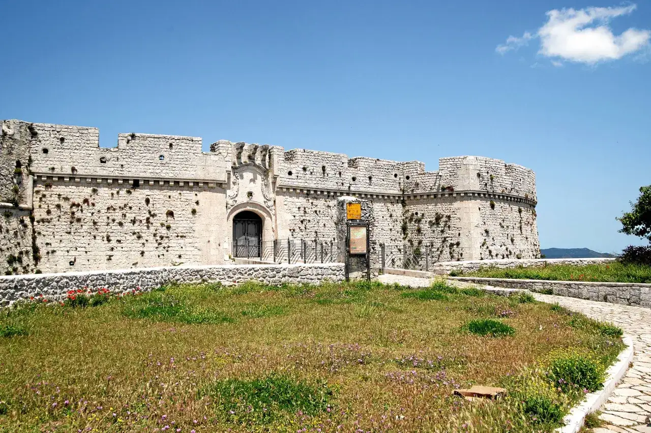 Castello normanno, parte del patrimonio UNESCO Puglia, con un prato fiorito e un cielo azzurro.