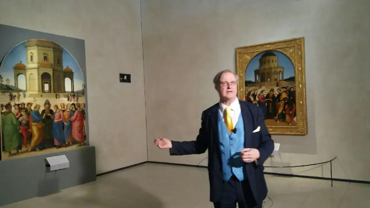 Un uomo parla davanti a due dipinti rinascimentali, uno attribuito a Raffaello e l'altro a Perugino, che raffigurano scene con architetture classiche e figure umane.
