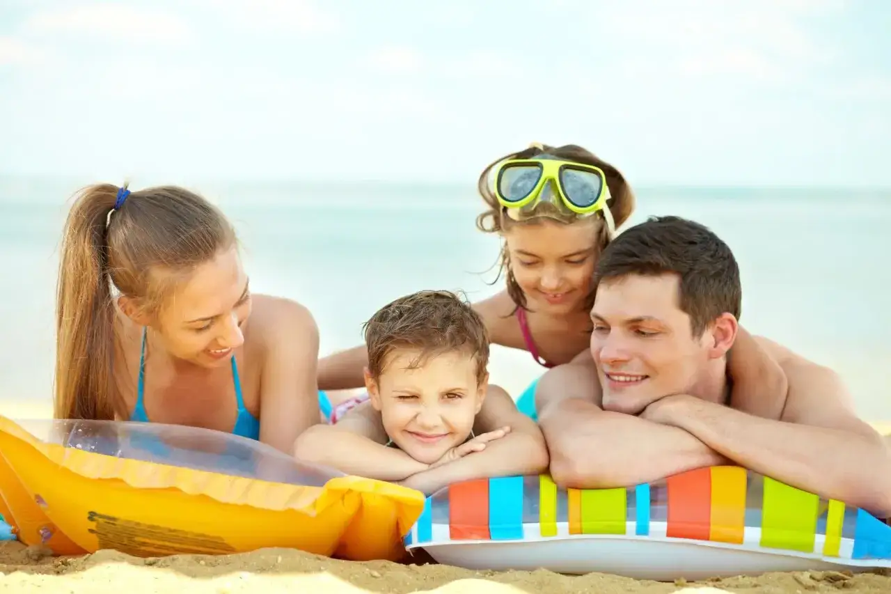 Famiglia felice in spiaggia, un esempio di cosa si fa a Ferragosto: relax e sorrisi tra gonfiabili e mare.