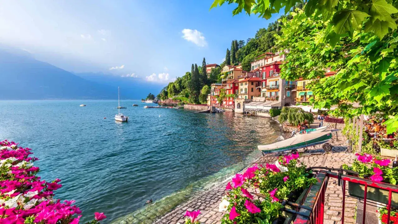 Un villaggio colorato sul lago, con barche e fiori rosa. Un'ottima idea per sapere dove andare ad aprile per godersi la primavera.