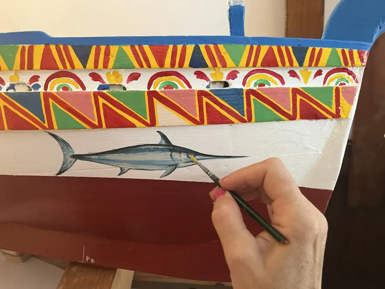 Mano dipinge un pesce spada su una barca colorata, un'espressione di tipica bellezza siciliana.