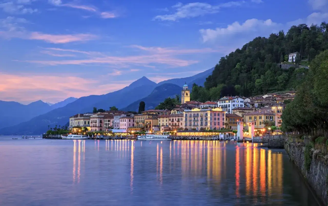 Bellagio, con le sue case colorate e il lago calmo, &egrave; un luogo incantevole. Ecco cosa vedere: il lungolago illuminato, le montagne sullo sfondo e la chiesa con il campanile.