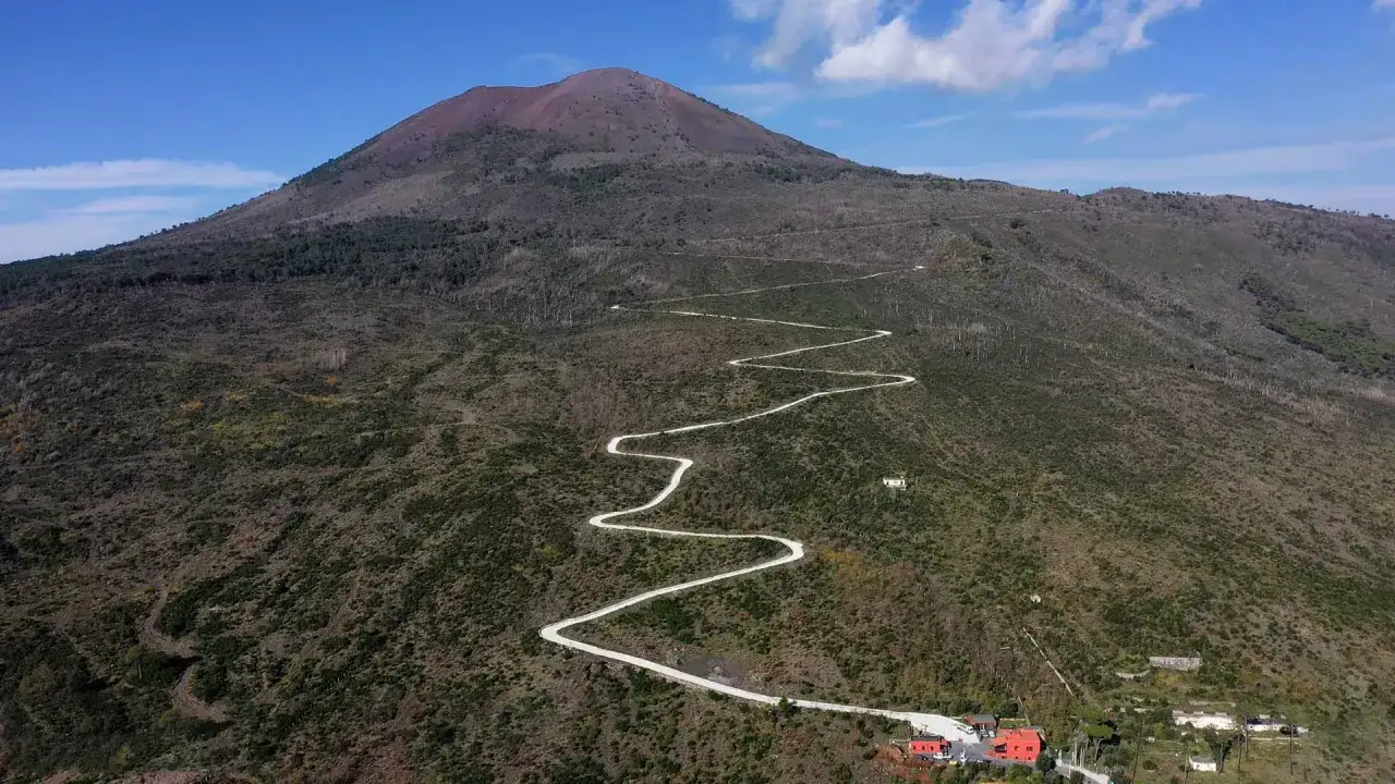 Strada tortuosa sale verso il Vesuvio, un invito a scoprire cosa vedere sul vulcano. Case rosse in basso.