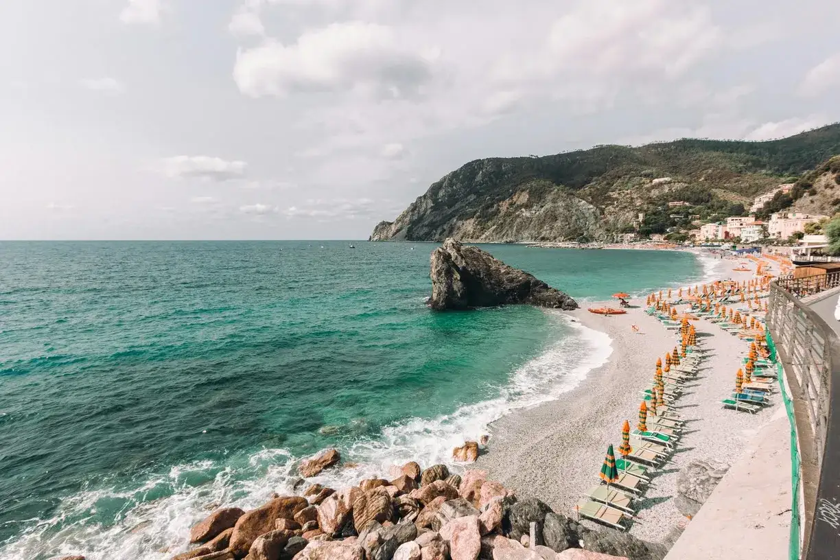 Spiaggia di ciottoli con lettini e ombrelloni colorati, mare turchese e scogliere. Un angolo di paradiso tra le genova spiagge più belle.