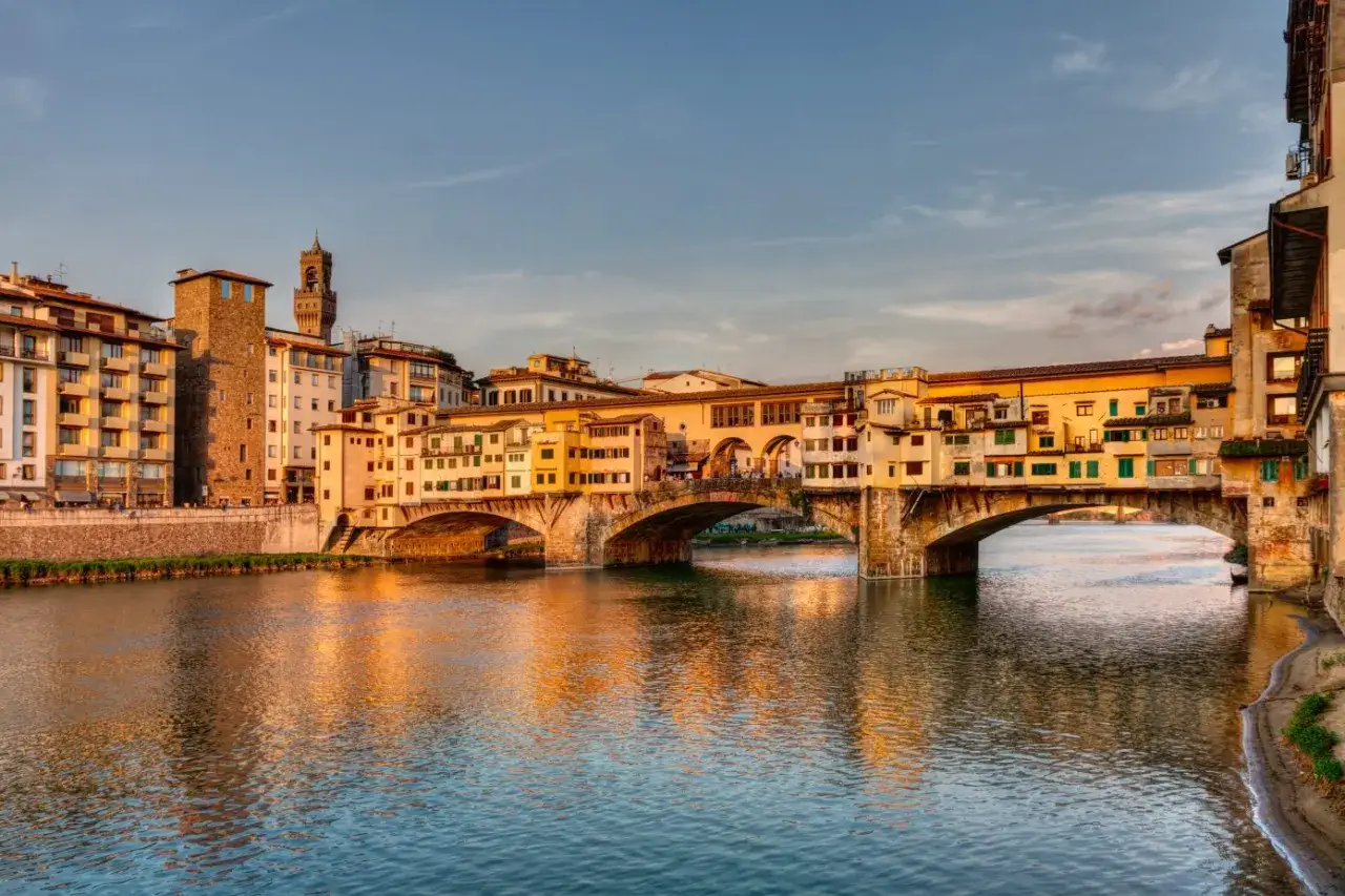Ponte Vecchio, uno dei simboli di Firenze, con le sue botteghe dorate al tramonto e il fiume Arno che riflette la luce.