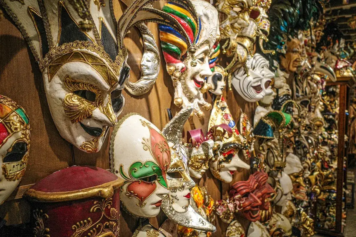 Una parete piena di maschere di carnevale romane, riccamente decorate, pronte per un ballo in maschera.