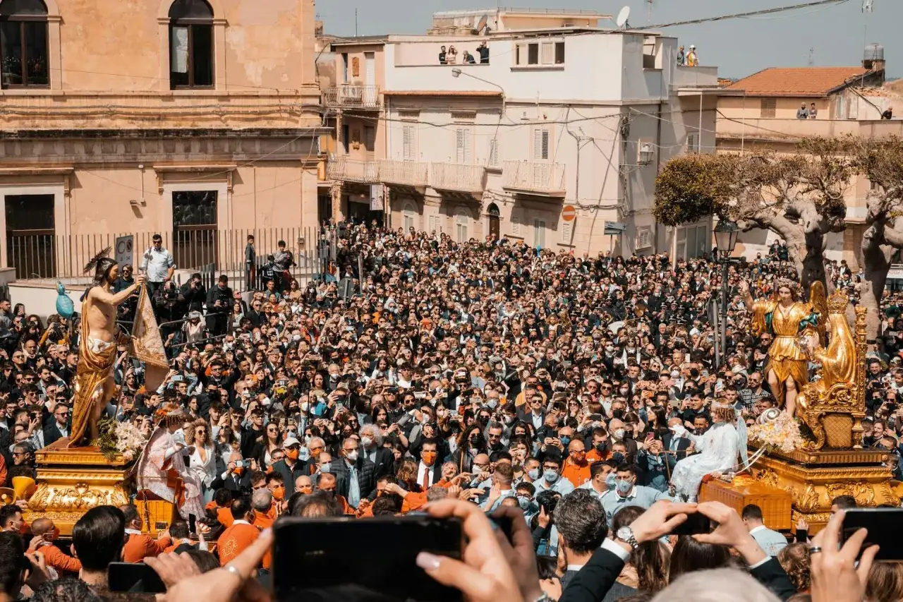 Una folla immensa partecipa a una processione religiosa, mostrando cosa si festeggia a Pasqua con statue dorate e devozione.