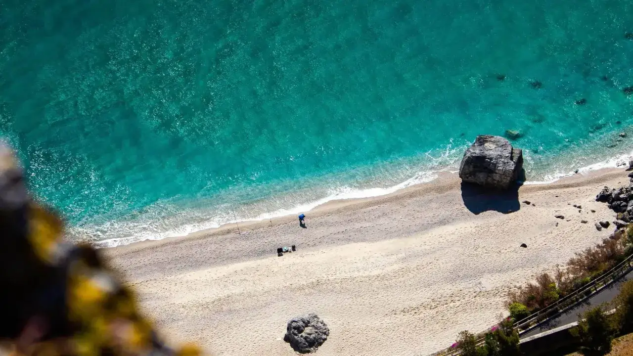 Un uomo pesca su una spiaggia di sabbia dorata, bagnata da un mare bello in Liguria dalle acque cristalline e turchesi.