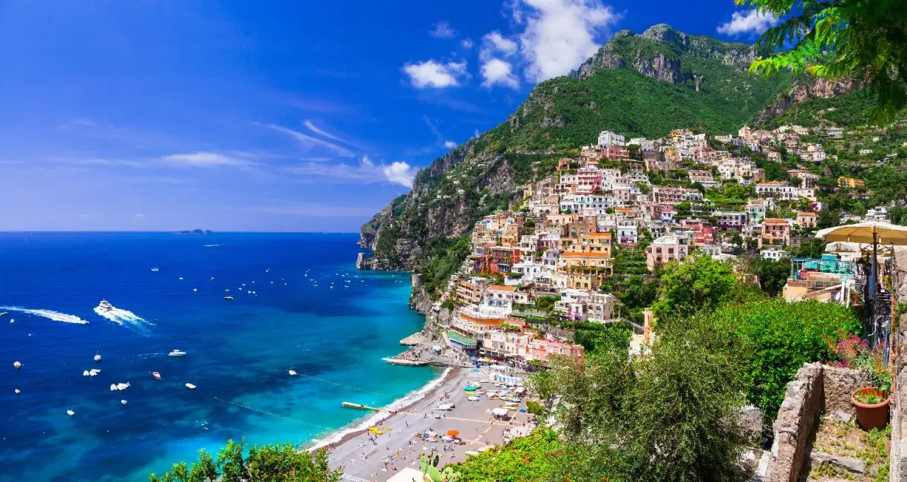 Positano, gioiello del mare in Campania, con case colorate aggrappate alla scogliera e barche che solcano le acque cristalline.