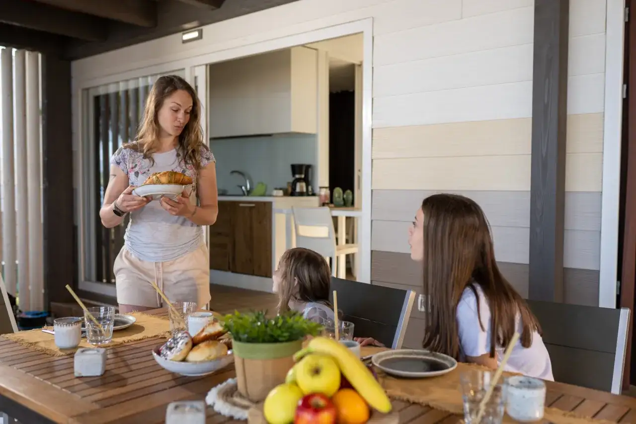 Una donna porta croissant a tavola, dove due bambine aspettano la colazione. Un momento di