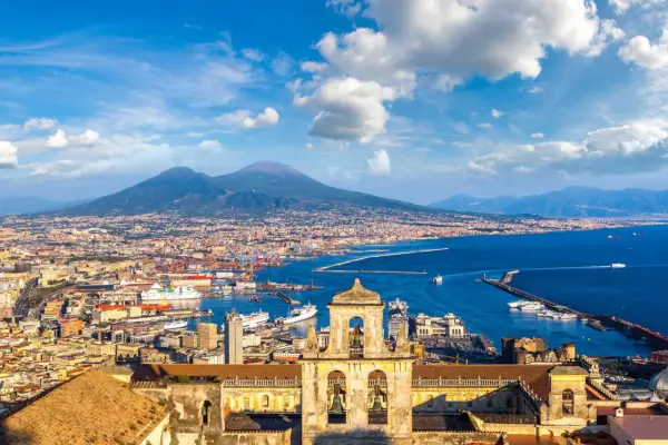 Vista di Napoli con il Vesuvio sullo sfondo, un porto vivace e un campanile antico. Un gioiello tra i siti UNESCO Campania.
