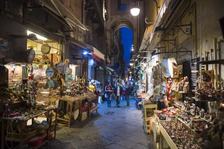 La via di San Gregorio Armeno, Napoli, illuminata di sera, con botteghe artigiane piene di presepi e statuine.