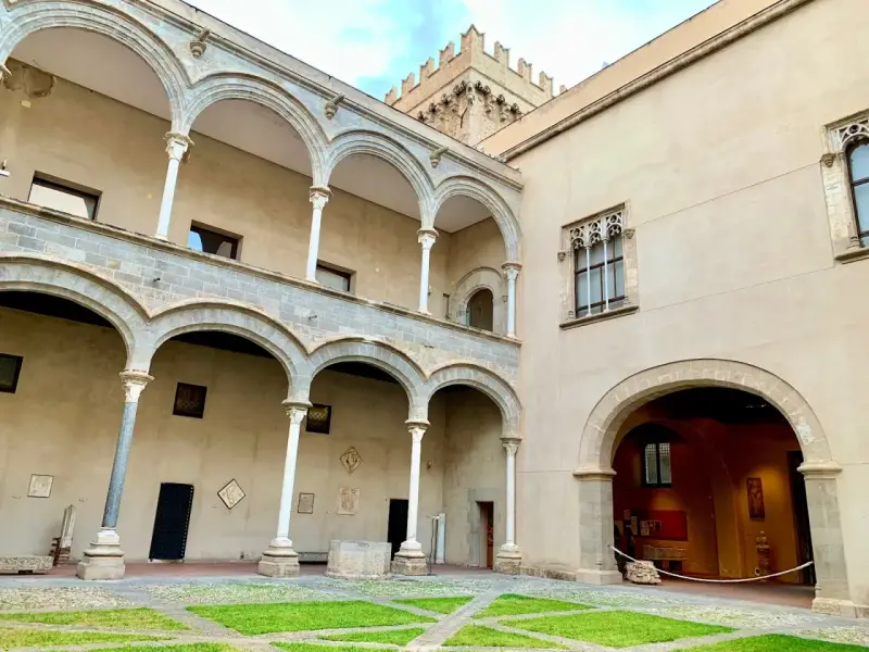 Cortile di Palazzo Abatellis, con arcate sovrapposte, finestre gotiche e opere d'arte esposte.